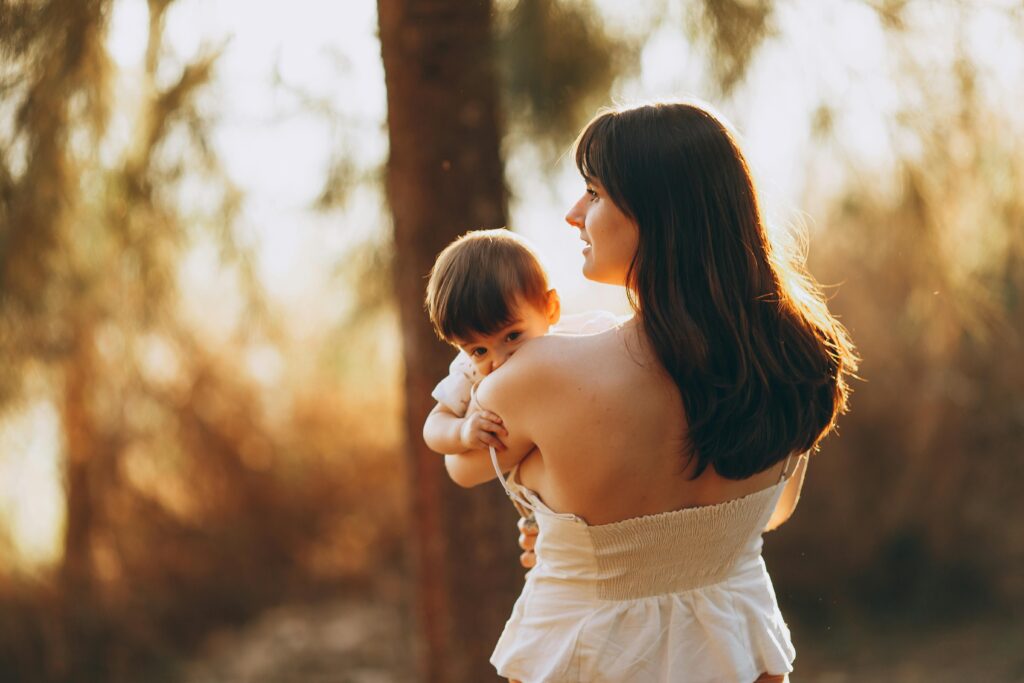 A mother lovingly holds her baby in a serene forest setting during sunset.